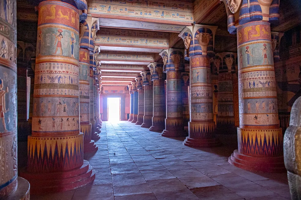 Decorated temple hall with painted columns leading to a bright doorway