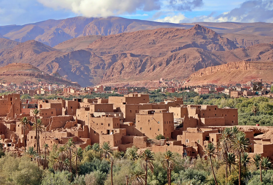 Mud-brick village with palm trees in a desert valley below rocky mountains