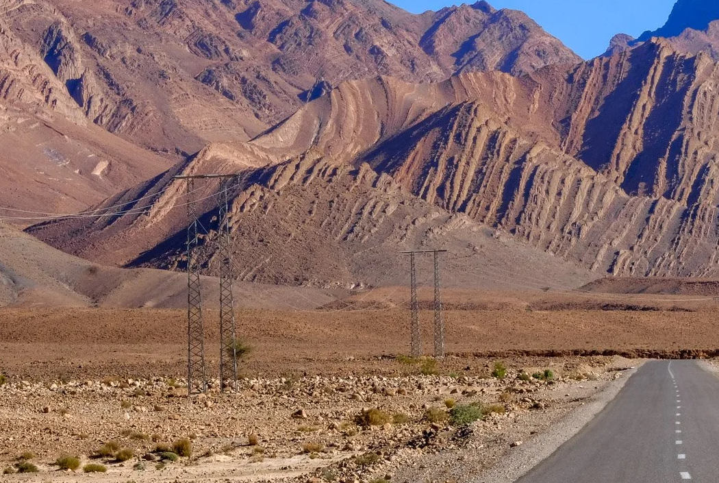 Desert road beside rugged mountains with power lines crossing the valley