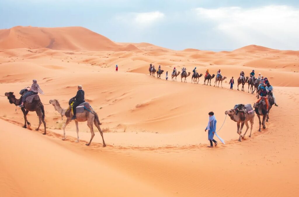 Camel caravan with riders crossing sand dunes in the desert